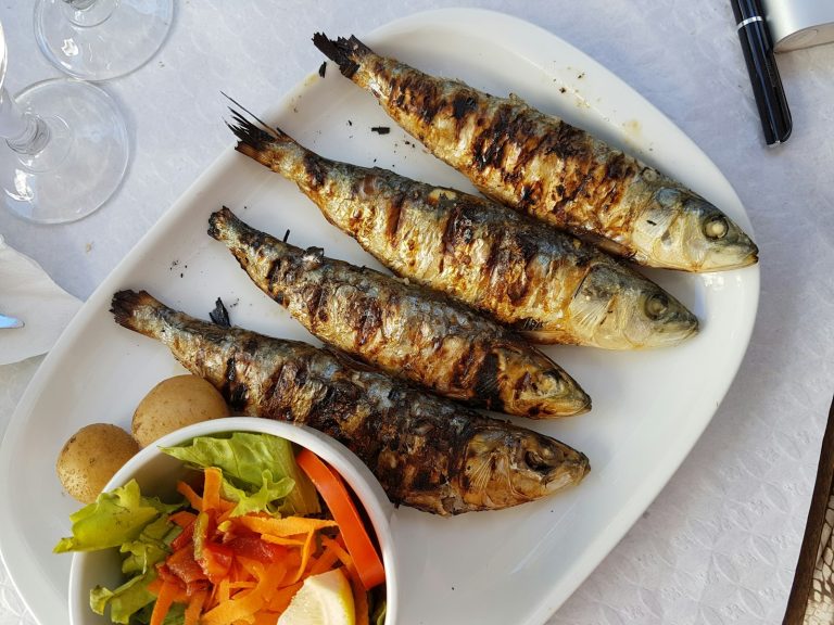 Keptos sardinės baltoje lėkštėje su salotomis ir bulvėmis
